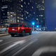 A rear view of a big red Tahoe driving on a nighttime downtown street.